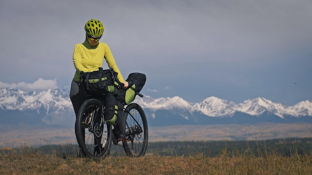 The woman travel on mixed terrain cycle touring with bikepacking The traveler journey with bicycle bags Sport tourism bikepacking bike sportswear in green black colors Mountain snow capped