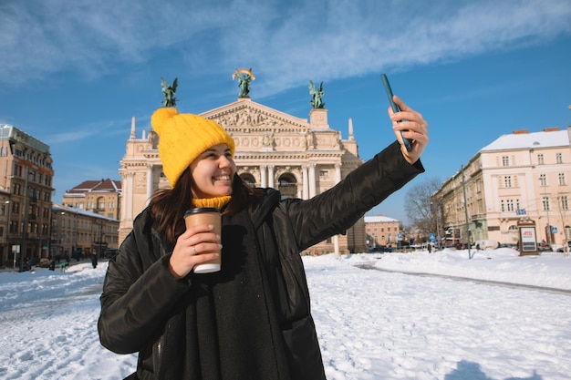 Woman traveler drinking coffee to go taking selfie in front of opera building