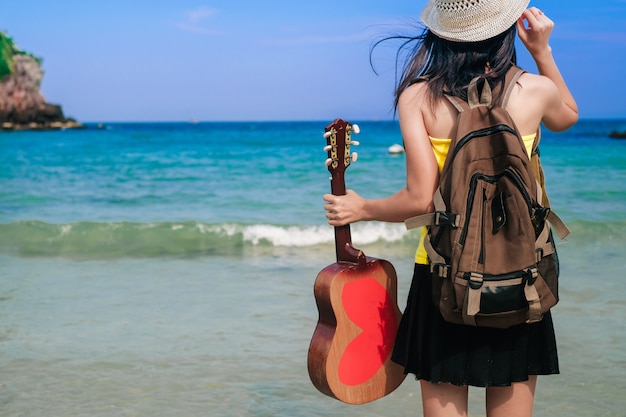 woman traveler have a bag and guitar standing on the beach