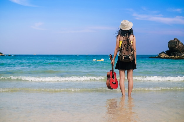 woman traveler have a bag and guitar standing on the beach