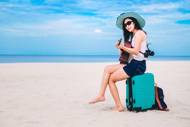 Woman traveler have a baggage and playing guitar on the beach