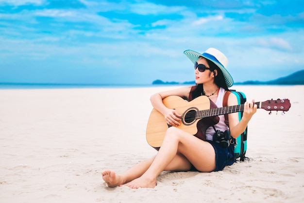 Woman traveler have a baggage and playing guitar on the beach