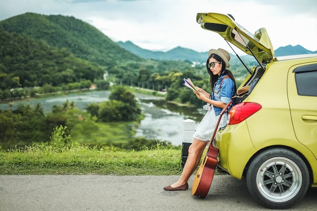 woman traveler sitting on hatchback of car and looking at the map for find the way on vaca