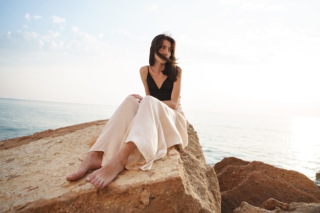 Woman traveler sitting near sea on cliff injoying view of sea and nature