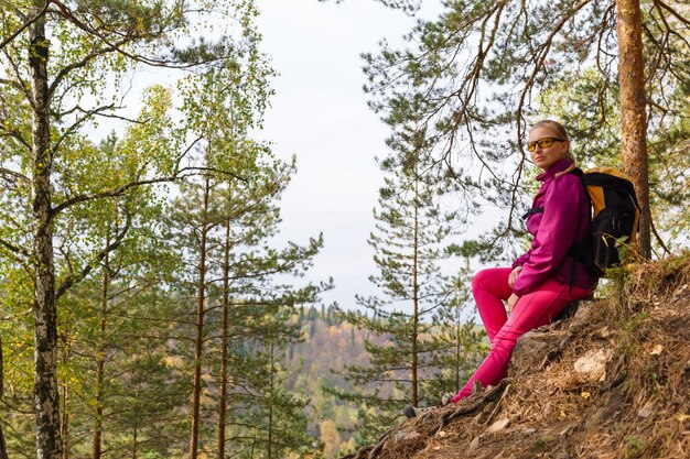 Woman traveler sitting resting on a stone on a mountainside among the autumn forest