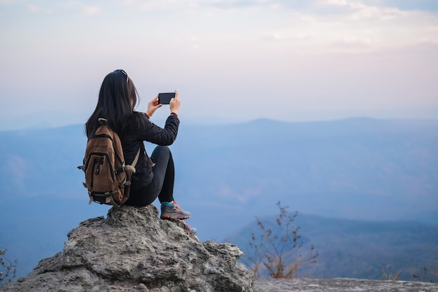 Woman traveler standing on top of the mountain and taking photo view of nature on holiday.