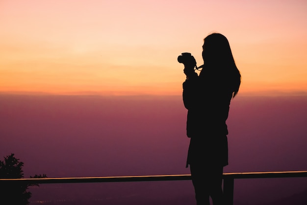 Woman traveler standing on top of the mountain and taking photo view of nature on holiday.