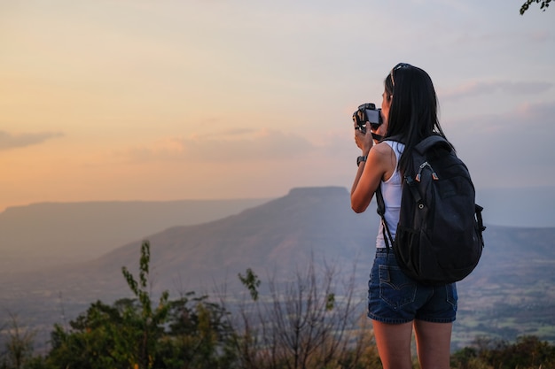 Woman traveler standing on top of the mountain and taking photo view of nature on holiday.