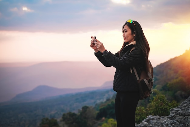 Woman traveler standing on top of the mountain and taking photo view of nature on holiday.