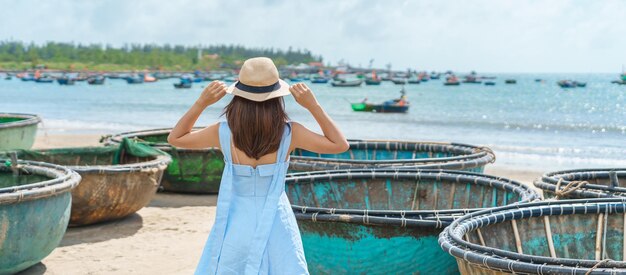 Woman traveler visiting at My Khe beach and sightseeing basket finishing boats Tourist with blue dress and hat traveling in Da Nang city Vietnam and Southeast Asia travel concept