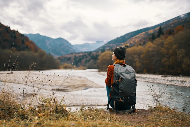 Woman traveler with a backpack on her back gestures with her hands and looks at the mountains in the distance