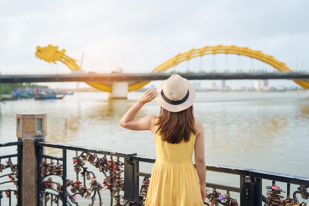 Woman Traveler with yellow dress visiting in Da Nang Tourist sightseeing the river view with Dragon bridge at love lock bridge Landmark and popular Vietnam and Southeast Asia travel concept