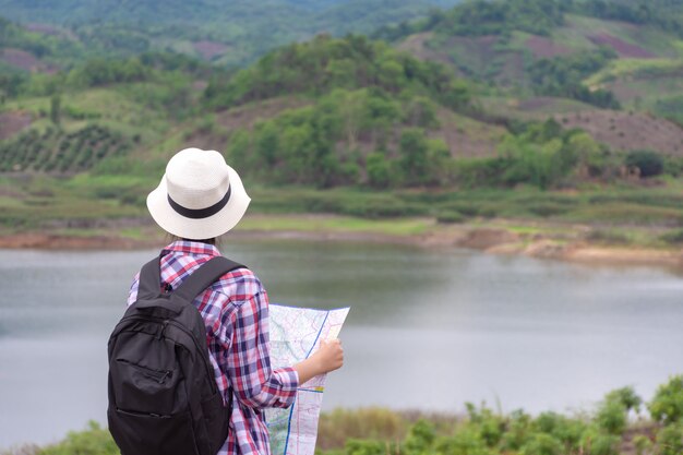 Woman traveling with backpacker holding map looking at mountain and lake