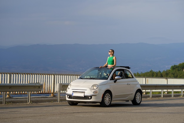 Woman traveller enjoys rocky landscapes above clouds high in mountains from small convertible car