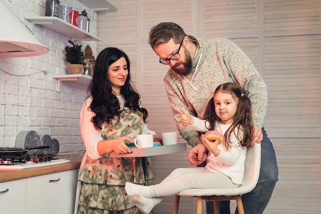 A woman treats her daughter and husband with tea and donuts