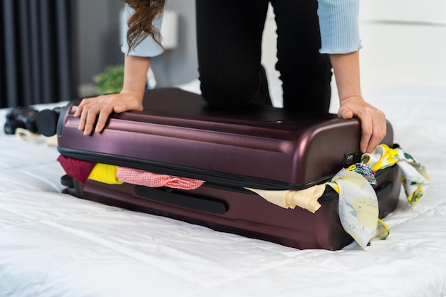 Woman trying to close overfilled suitcase on bed