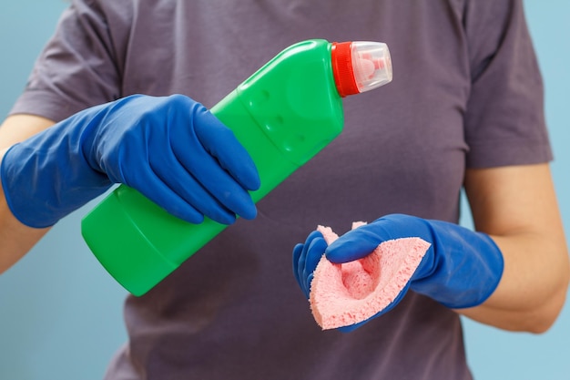 Woman in a tshirt holding a plastic bottle of washing liquid and a rag on the blue background