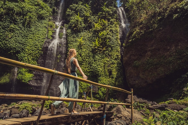 Woman in turquoise dress at the Sekumpul waterfalls in jungles on Bali island Indonesia Bali Travel Concept