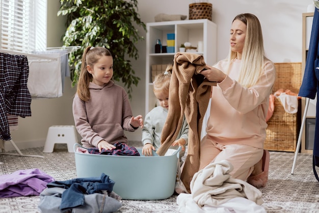 A woman and two daughters with blond and bronze hair fold clean laundry taken out of the dryer