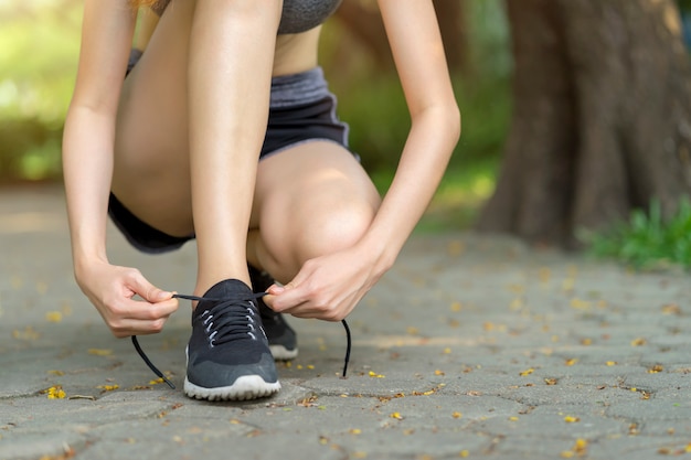 Woman tying shoe laces. Female sport fitness runner getting ready for jogging at garden.