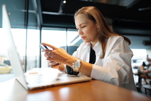 Woman typing text message on smart phone while sitting in a cafe