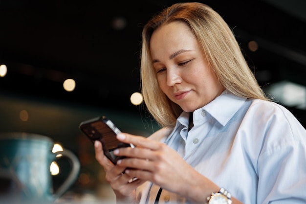 Woman typing text message on smart phone while sitting in a cafe