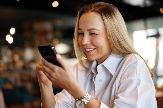 Woman typing text message on smart phone while sitting in a cafe