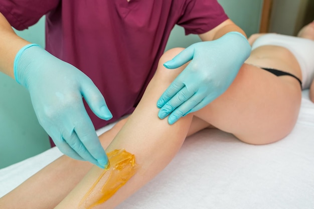 Woman undergoing leg hair removal procedure with sugaring paste in salon Skin care remove hair with sugar paste