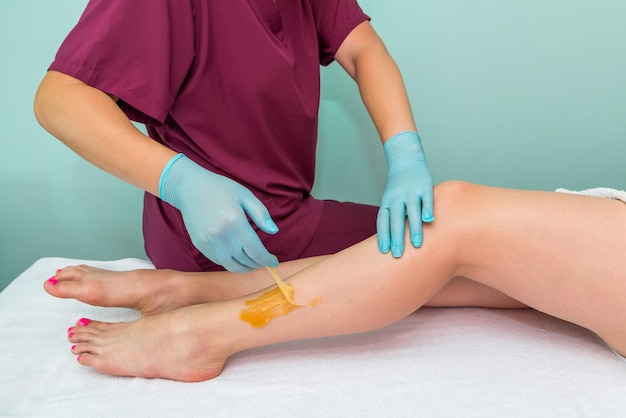 Woman undergoing leg hair removal procedure with sugaring paste in salon Skin care remove hair with sugar paste