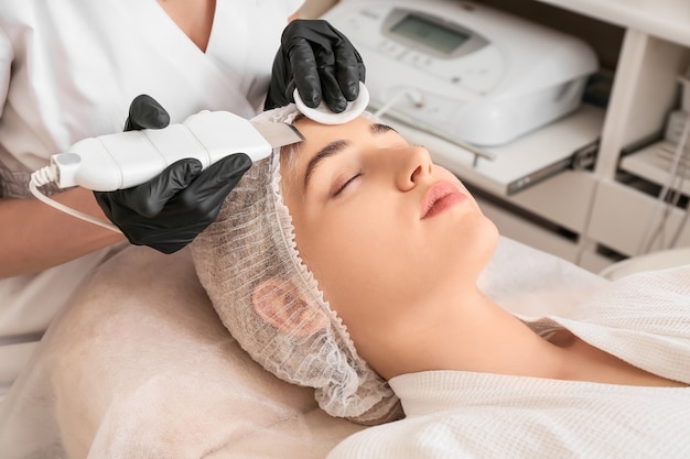 Woman undergoing procedure of facial peeling in beauty salon