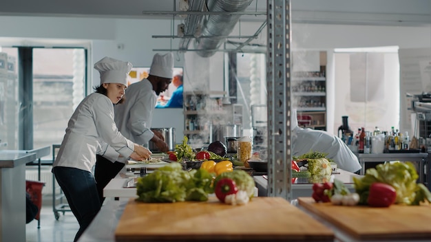 Woman in uniform cooking delicious dish on kitchen stove, doing meal preparations with ingredients and utensils. Gourmet chef preparing professional cuisine recipe, culinary service.