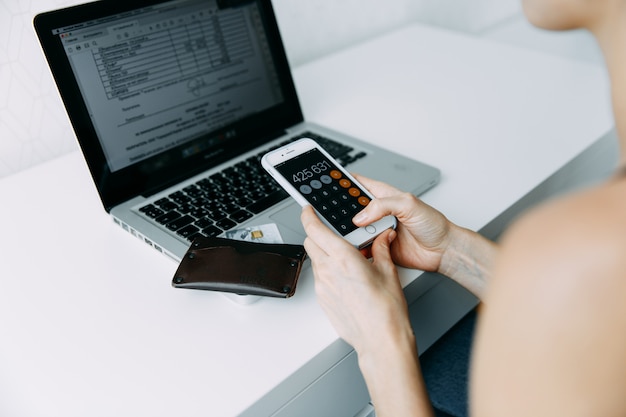 woman use phone with open calculator and holding credit card with shopping online near laptop 