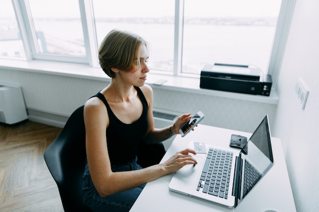 woman use phone with open calculator and holding credit card with shopping online near laptop 