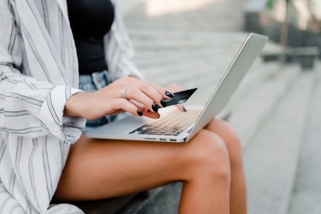 Woman uses bank credit card and laptop outdoors