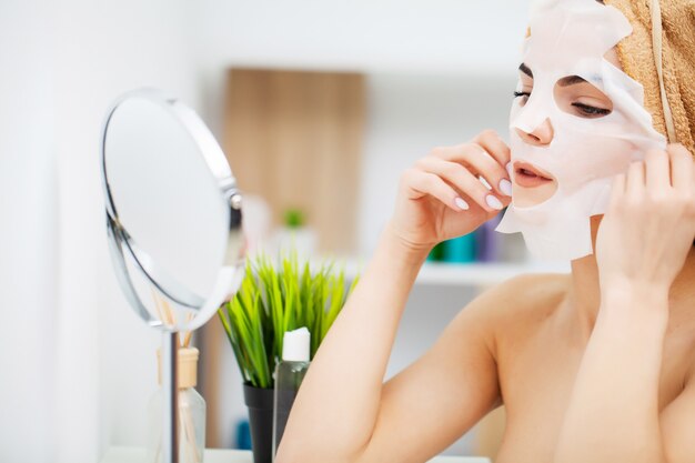 A woman uses a face care mask in the bathroom