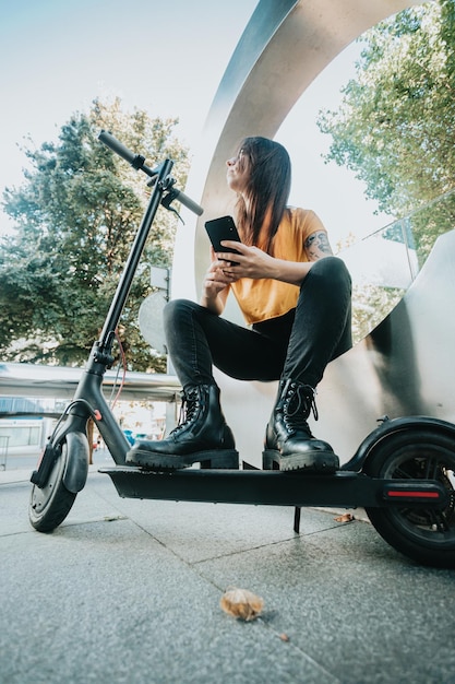 Woman uses her smartphone while moving with her electric scooter around the city street New ecofriendly transport woman using phone cell for unlocking electric push scooter