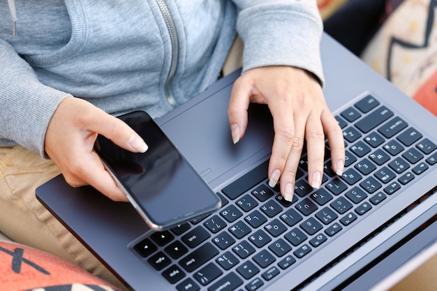 Woman uses mobile phone and notebook computer outdoors. background is blurred.