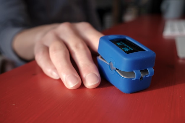 Woman uses a pulse oximeter to measure pulse rate and blood oxygen levels on a red table