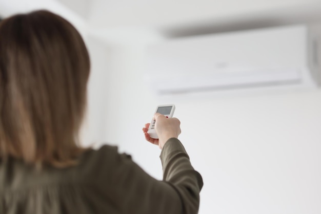 Woman uses remote control to adjust air conditioner hanging on wall in office employee