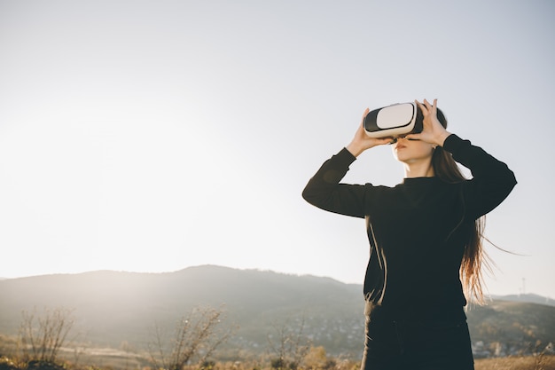 Woman uses virtual reality glasses at sunset. Evening time, twilight. Relax, entertainment and technology concept