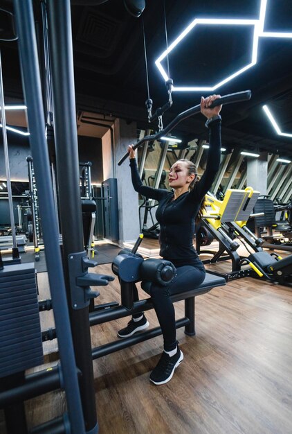 Woman using cable machine in gym A woman engages in strength training using a cable machine showcasing her determination in a wellequipped fitness center