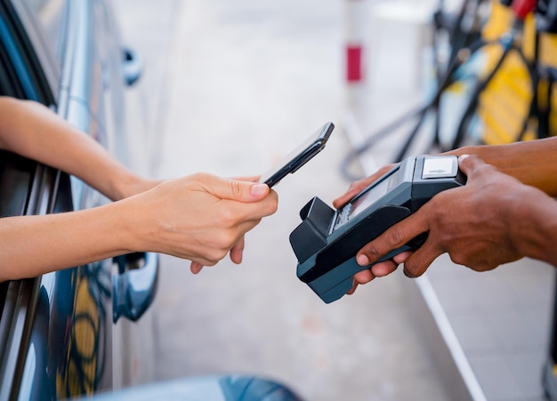 Woman using contactless payment by mobile phone with QR code at car filling station