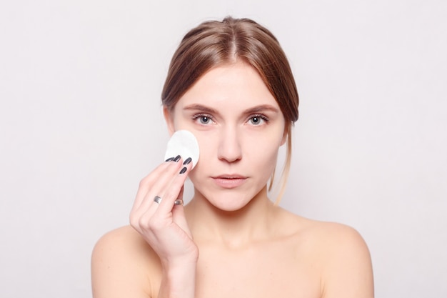 Woman using cotton pad. Happy smiling beautiful young woman cleaning skin by cotton pad. light background. Beautiful Spa Woman Smiling. Perfect Fresh Skin. Youth and Skin Care Concept