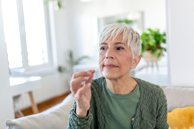 Woman using cotton swab while doing coronavirus PCR test at home. Woman using coronavirus rapid diagnostic test. Mature woman at home using a nasal swab for COVID-19.