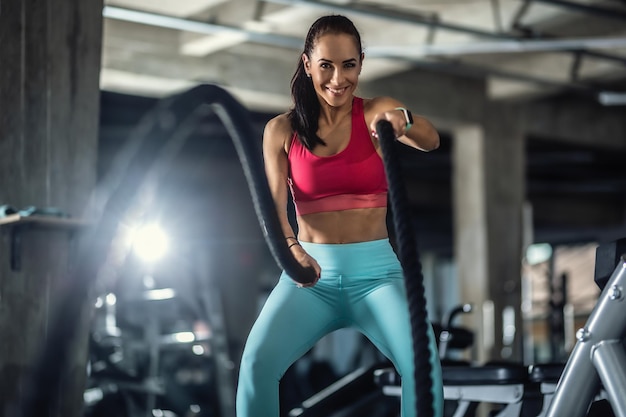 Woman using crossfit ropes works out in the gym, smiling.