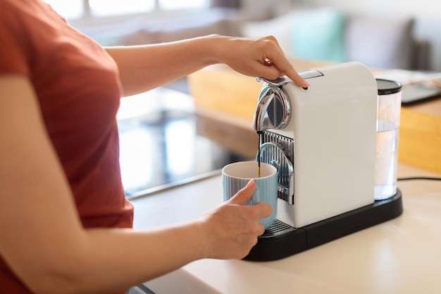 Woman using espresso machine in kitchen pouring coffee in cup