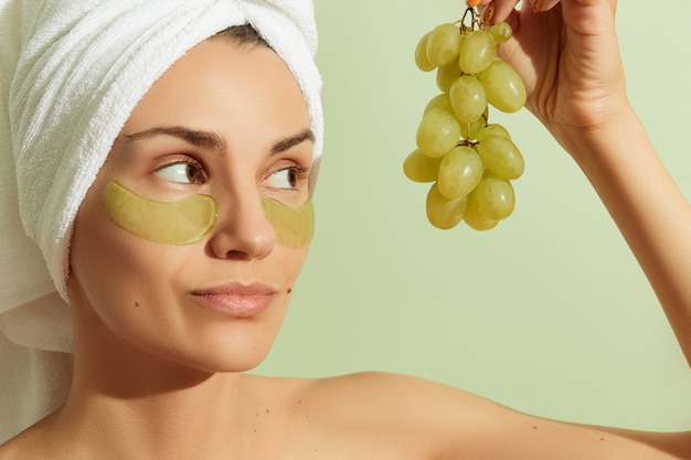 Woman using grapeseedbased eye patches on pastel green background