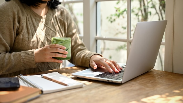 A woman using her laptop and enjoying with her iced matcha green tea at a coffee shop