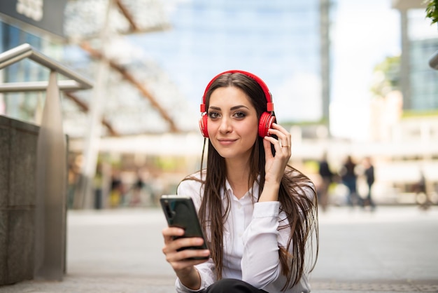 Woman using her mobile phone to listen music while sitting on stairs outdoor