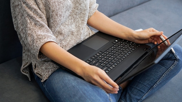 Woman using laptop with blank screen while sitting on sofa in home interior back view